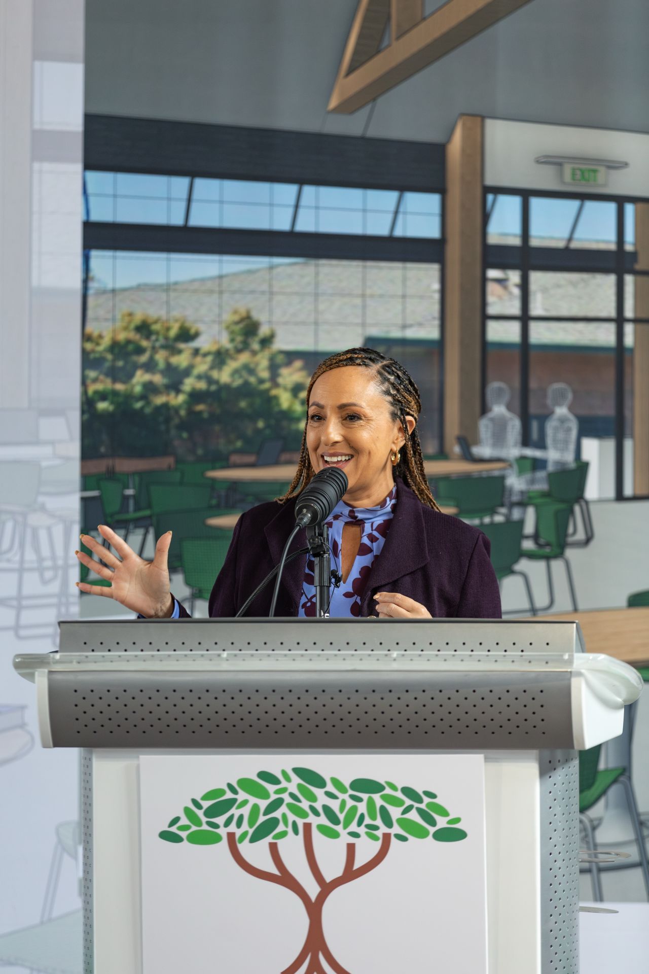 Roots Community Health leader speaking at a podium in front of renderings of the Young People's Wellness Center